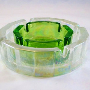 May include: A vintage ashtray set with a clear, iridescent outer ashtray and a bright green inner ashtray. The ashtrays have a geometric, octagonal shape. The glass has a reflective, shimmering quality.