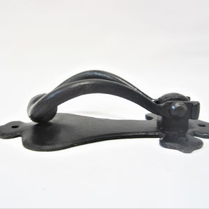 May include: A black, cast iron door knocker with a decorative handle and a stylized backplate. The handle is a twisted design, and the backplate has a floral shape with mounting holes.