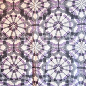 May include: A close-up of a fabric with a repeating geometric pattern. The design features overlapping shapes in shades of purple, gray, and white. The pattern creates a layered, textured effect, with a symmetrical, star-like motif.