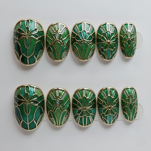May include: Set of ten oval-shaped, press-on nails. Each nail features a green and gold art deco design. The nails have a glossy finish and are arranged in two rows of five.