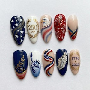 May include: A set of ten artificial nails with patriotic designs. The nails feature images of the American flag, an eagle, fireworks, the Statue of Liberty, and the text "250 USA" and "1776 2026". The color palette includes red, white, blue, and gold.