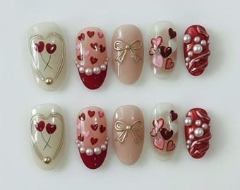 May include: A set of ten artificial nails with various designs. The nails feature heart and bow designs, with colors including red, pink, gold, and white. Some nails have pearl accents. The nails are oval-shaped.