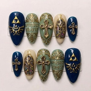 May include: A set of ten artificial nails in various designs. The nails feature a mix of colors, including blue, cream, and green, with gold accents. Designs include crosses, stained glass, and a gold emblem. The nails are oval-shaped.