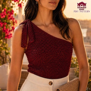 May include: A burgundy crochet one-shoulder top with a tie detail on the shoulder. The top is paired with cream-colored pants. The image also includes the text "DAGRAGO SHOP PDF / PATTERN".
