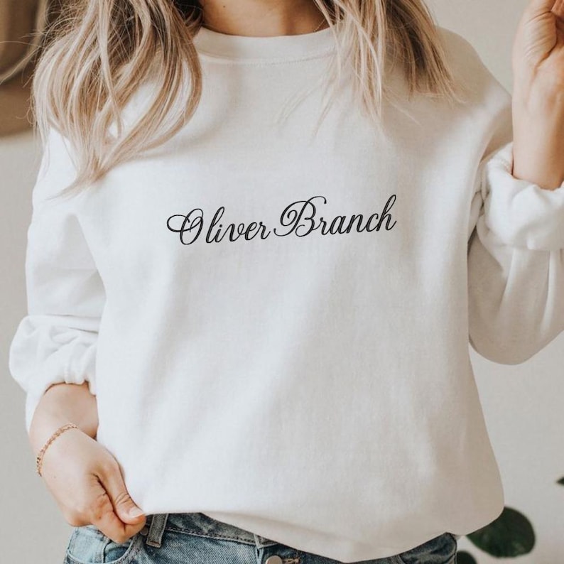 May include: A white long-sleeve crewneck sweatshirt featuring the text Oliver Branch printed in a black cursive script across the center of the chest. The garment has a standard fit with ribbed cuffs and a ribbed neckline, providing a clean look.