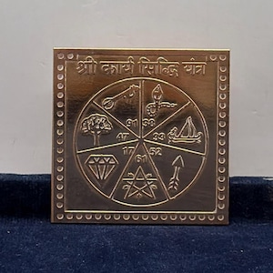Peut inclure: Une plaque carrée en métal doré portant l'inscription "श्री कार्य सिद्धि यंत्र" en haut. Le centre présente un motif circulaire divisé en six segments, chacun affichant des symboles gravés dont une clé, un serpent, un arbre, un bateau, un diamant et une flèche.