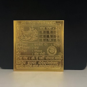 Puede incluir: Placa metálica cuadrada dorada con intrincados diseños grabados y texto en escritura extranjera. La placa presenta un diseño circular central y varias líneas de texto, probablemente de naturaleza religiosa o espiritual.