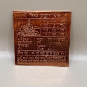 Könnte beinhalten: Quadratische Kupferplatte mit detaillierten Gravuren und Text in einer fremden Schrift. Die Platte zeigt ein zentrales Bild einer Gottheit, Zahlentafeln und zusätzlichen Text. Die Farbe ist ein warmer Kupferton.