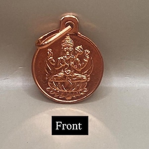 Puede incluir: Un colgante redondo de color cobre con una imagen en relieve detallada de una deidad sentada en una flor de loto. El colgante tiene un lazo en la parte superior para colgar y la palabra "Front" se muestra en un rectángulo negro en la parte inferior.