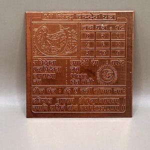 Puede incluir: Placa cuadrada de cobre con texto y símbolos grabados. La placa presenta una cuadrícula de números, ilustraciones y texto en escritura no inglesa. El diseño general es intrincado, con un enfoque en patrones detallados e iconografía religiosa.