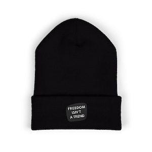May include: Black beanie hat with a folded brim. A small, rectangular patch on the front of the hat displays the text "FREEDOM ISN'T A TREND" in white letters.