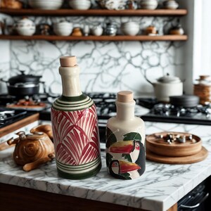 Hand-painted ceramic olive oil and vinegar bottles with cork stoppers, tropical toucan and red palm leaf designs on marble kitchen counter.
Artisan pottery cruet set, Mediterranean kitchen decor, unique handmade ceramic oil dispensers.
Decorative ceramic bottles for olive oil, vinegar, or balsamic, rustic boho farmhouse kitchen style.