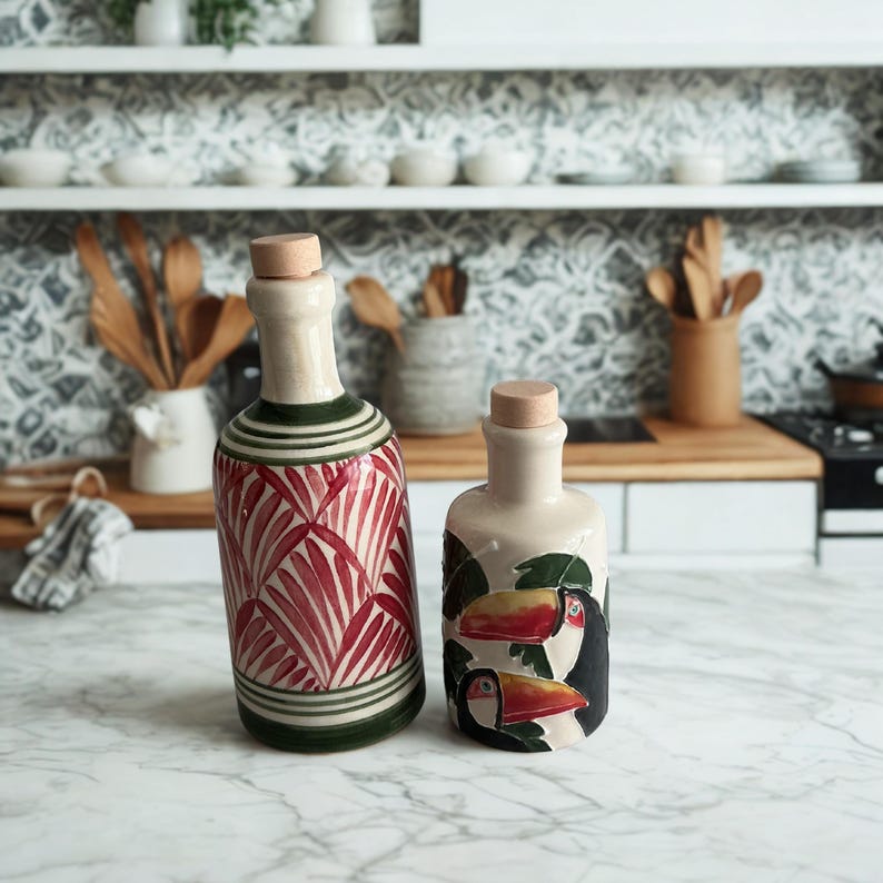 Hand-painted ceramic olive oil and vinegar bottles with cork stoppers, tropical toucan and red palm leaf designs on marble kitchen counter.
Artisan pottery cruet set, Mediterranean kitchen decor, unique handmade ceramic dispensers.
Decorative ceramic oil bottles, rustic boho style kitchenware, perfect for olive oil, vinegar, or balsamic.