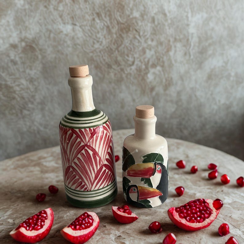 Decorative ceramic bottles for olive oil, vinegar, or balsamic, boho rustic table styling with pomegranate accents.
Handmade pottery cruet set, eco-friendly ceramic kitchenware, perfect for housewarming or gourmet gift ideas.
Mediterranean style ceramic bottles with artistic red palm leaf and toucan bird motifs, ideal for rustic farmhouse kitchens.
