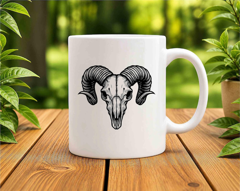 May include: White ceramic mug featuring a detailed black illustration of a ram skull. The skull has large, curved horns and is centered on the mug. The mug has a standard handle and is set on a wooden surface.