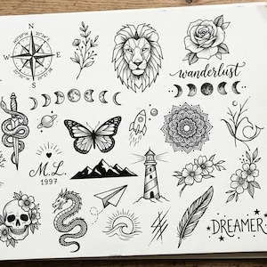 May include: A sketchbook page featuring various black ink tattoo designs. The illustrations include a swallow, compass, lion, rose, mandala, and other nature-inspired and celestial elements. The word "wanderlust" is written in cursive.