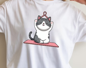 Peut inclure: T-shirt blanc avec un chat de dessin animé faisant du yoga. Le chat est gris et blanc, assis sur un tapis de yoga rose avec les pattes levées. Un ruban rose est au-dessus de la tête du chat. Le motif est centré sur le t-shirt.