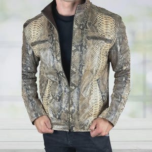 May include: A snakeskin-effect leather jacket with a full-length zip and two zipped chest pockets. The jacket has a brown collar and a black interior. The jacket is worn over a black shirt and paired with dark blue jeans.