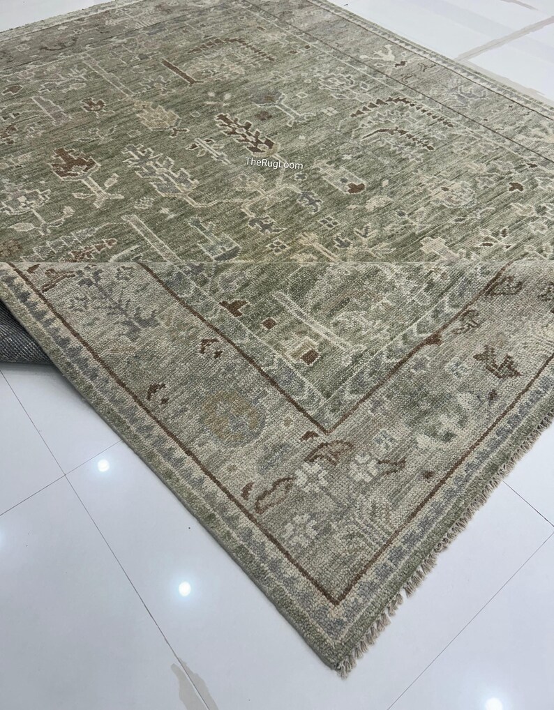 May include: A sage green area rug with an intricate, traditional pattern. The rug features a central field with floral and geometric motifs in shades of brown, beige, and gray. A detailed border frames the design. The Rug Loom is printed on the rug.
