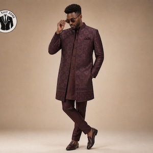 Op de afbeelding: Een bordeauxrood pak met een bloemmotief. Het pak bestaat uit een lange jas, een overhemd en een bijpassende broek. De persoon op de foto draagt een zonnebril en bruine leren schoenen. Het logo van "The Suit Zone" staat linksboven.