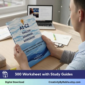 Può includere: Quaderno di grammatica inglese A1-C2 con copertina blu e bianca, tenuto in mano da una persona. Il quaderno include il testo "Beginner to Proficiency Curriculum" e "300 Worksheets with Study Guides". Un laptop e altra cancelleria sono sullo sfondo.