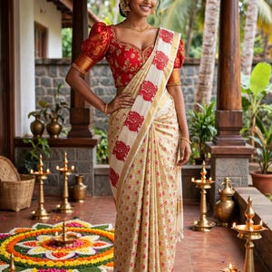 May include: A traditional saree featuring a cream-colored fabric with a repeating gold pattern and a wide white border adorned with red peacock motifs. The ensemble includes a short-sleeved red blouse with intricate gold embroidery and gold trim.