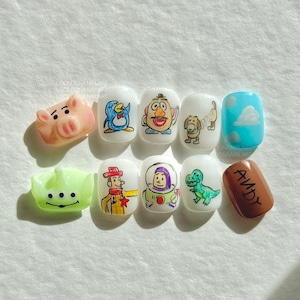 Può includere: Un set di dieci nail art con personaggi del film d'animazione Toy Story. I disegni includono un maiale rosa, un pinguino blu, Mr. Potato, un cane, un'unghia blu con nuvole, un alieno verde, Woody, Buzz Lightyear, un dinosauro verde e un'unghia marrone con il nome "Andy".