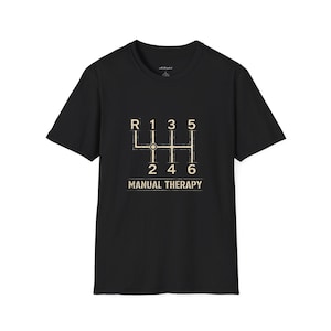 以下が含まれることがあります： 黒いTシャツ。手動変速機のギアパターンを図示。数字はR、1、2、3、4、5、6。ギアパターンの下に「MANUAL THERAPY」の文字。