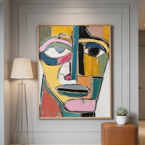 May include: Abstract face art print in a wooden frame. The artwork features bold colors including yellow, blue, pink, and green. The painting is displayed in a modern interior with a floor lamp and a leather ottoman.