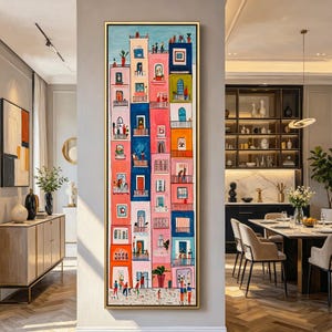 Op de afbeelding: Een kleurrijk, verticaal schilderij van een stadsgezicht met gebouwen in roze, blauw en oranje. Elk gebouw heeft ramen, balkons en mensen. Het kunstwerk is goudomrand en hangt aan een grijze muur.
