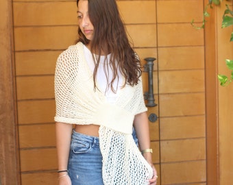 May include: A white crochet shawl with a loose, open weave. The shawl is draped over a person's shoulders and tied at the waist. The shawl is made of a soft, lightweight yarn.