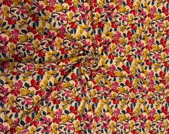 May include: Close-up of a fabric with a repeating floral pattern. The design features small flowers in shades of red, pink, and yellow, with dark blue leaves, set against a cream-colored background. The fabric is gathered in the center.
