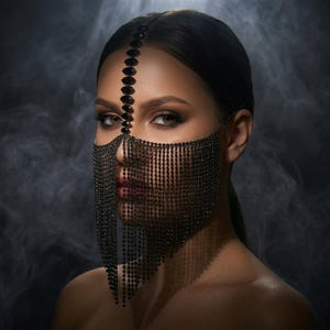 May include: A black, jeweled face mask with a matching headpiece. The mask is made of small, dark beads that drape over the face and neck. The headpiece is a line of dark jewels. The background is a smoky gray.