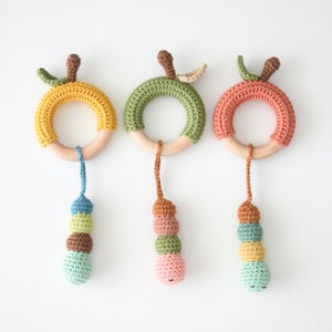 May include: Three crocheted wooden ring teethers with colorful crocheted beads hanging from each ring. The rings are yellow, green, and orange. The beads are blue, green, brown, and pink.