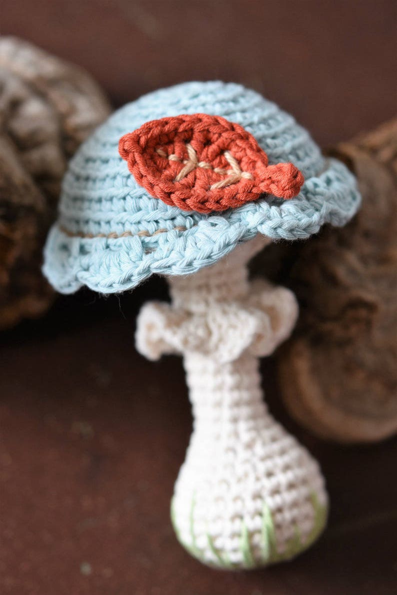 May include: A crocheted mushroom toy with a light blue cap and a white stem. The cap has a small orange leaf detail.