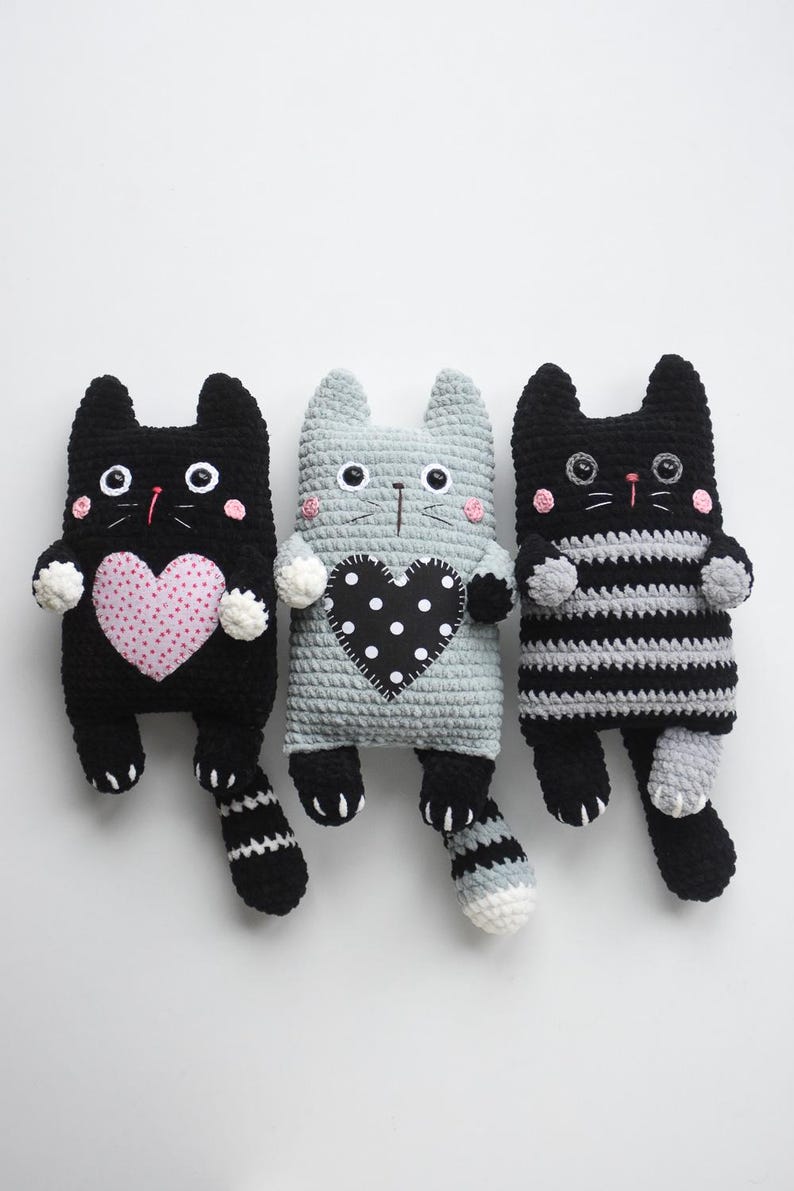 Pode incluir: Tr&ecirc;s bonecas de gato de croch&ecirc; feitas &agrave; m&atilde;o em preto, cinza e listras pretas e brancas. Cada gato tem um desenho em forma de cora&ccedil;&atilde;o no peito, com bolinhas rosa no gato preto. Os gatos t&ecirc;m olhos de bot&atilde;o e bochechas rosadas.