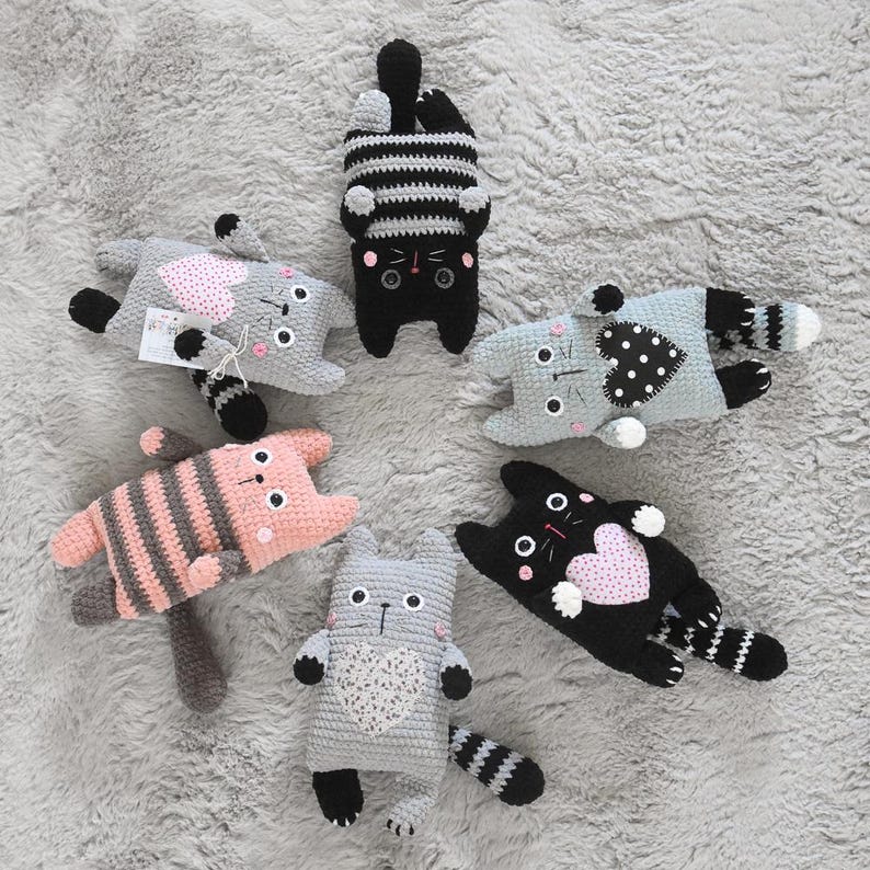 Pode incluir: Uma cole&ccedil;&atilde;o de brinquedos de gato feitos &agrave; m&atilde;o em croch&ecirc; em v&aacute;rias cores e padr&otilde;es. Os gatos s&atilde;o cinza, preto, rosa e azul, com detalhes listrados e em forma de cora&ccedil;&atilde;o. Cada gato tem um design &uacute;nico.