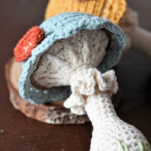 May include: Two crocheted mushroom toys. One is blue with a red flower and the other is yellow with a purple flower. Both have white stems.