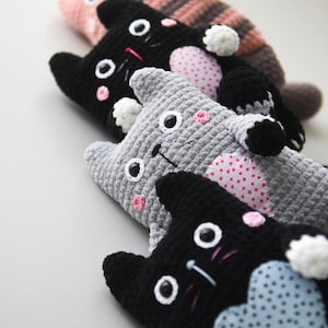 Pode incluir: Uma cole&ccedil;&atilde;o de bichos de pel&uacute;cia de gato de croch&ecirc; feitos &agrave; m&atilde;o em v&aacute;rias cores. Os gatos t&ecirc;m olhos brancos, bochechas rosadas e rostos bordados. Alguns gatos t&ecirc;m cora&ccedil;&otilde;es estampados na barriga, e outros t&ecirc;m corpos listrados ou s&oacute;lidos.