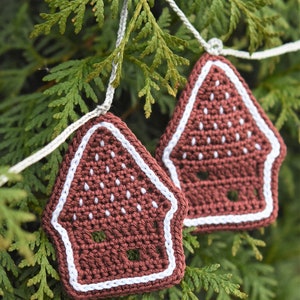 May include: A garland of crocheted gingerbread house decorations in brown and white, hanging from a green evergreen tree branch.