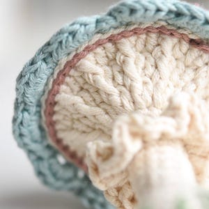 May include: A crocheted mushroom toy with a light blue, pink, and white color scheme. The mushroom has a textured, ribbed top and a ruffled bottom.