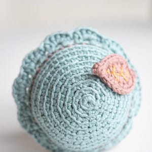 May include: A crocheted ball toy in light blue with a pink leaf detail. The leaf has a yellow embroidered design.