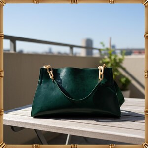 May include: A dark green leather tote bag with cream-colored chain handles. The bag has a curved top and a single handle. The background shows a city skyline and a plant in a pot.