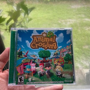 May include: A clear plastic case containing the "Animal Crossing: New Leaf" soundtrack CD. The cover art features cartoon characters in a colorful village scene. The ESRB rating is visible, along with the Nintendo logo.