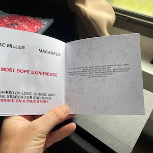 Pu&ograve; includere: Libretto CD aperto per l'album di Mac Miller, "Macadelic". La copertina recita "A Most Dope Experience" in testo rosso, con il tagline "Ispirato dall'amore, dalla droga e dalla ricerca dell'euforia. Basato su una storia vera." La custodia del CD &egrave; visibile sullo sfondo.