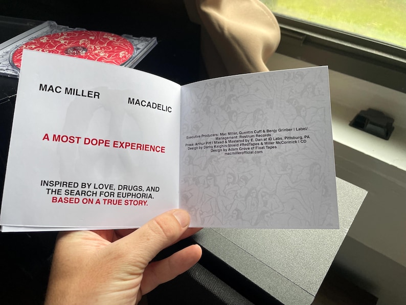 Pu&ograve; includere: Libretto CD aperto per l'album di Mac Miller, "Macadelic". La copertina recita "A Most Dope Experience" in testo rosso, con il tagline "Ispirato dall'amore, dalla droga e dalla ricerca dell'euforia. Basato su una storia vera." La custodia del CD &egrave; visibile sullo sfondo.