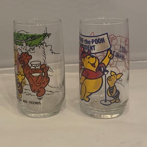 May include: Two clear glass tumblers featuring Winnie the Pooh characters. One glass has a scene with Tigger and Pooh, the other has Pooh holding a sign that says "Winnie-the-Pooh President".