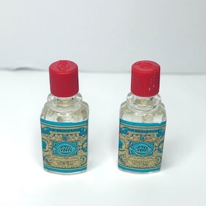 May include: Two small clear glass bottles of 4711 Echt Kolnisch Wasser cologne, each featuring a bright red screw-top cap and a rectangular label with blue and gold ornate detailing, including the text 4711 and Echt Kolnisch Wasser.