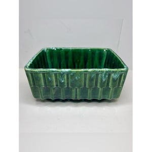 May include: A rectangular ceramic bowl featuring a deep emerald green glaze with lighter green highlights along the top rim. The exterior surface is decorated with a repeating vertical ribbed pattern that extends from the base to the upper edge.