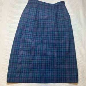May include: A knee-length skirt with a plaid pattern in shades of blue, teal, and purple. The skirt has a button closure at the waist. The fabric appears to be a woven material, suitable for cooler weather.